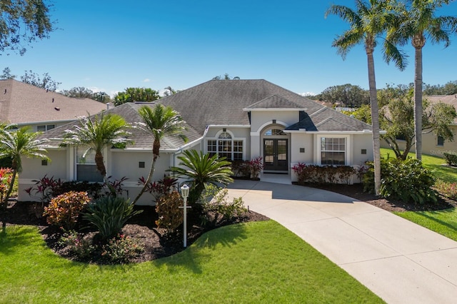 view of front of home featuring french doors, roof with shingles, stucco siding, driveway, and a front lawn