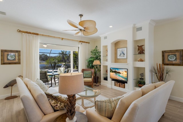 living area featuring built in features, light wood finished floors, ornamental molding, ceiling fan, and baseboards