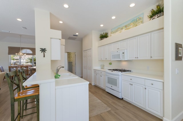 kitchen with pendant lighting, white cabinets, a sink, white appliances, and a peninsula