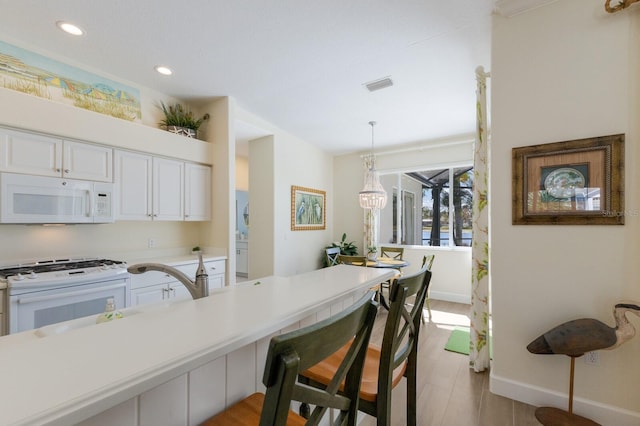 kitchen with light countertops, hanging light fixtures, visible vents, white cabinetry, and white appliances