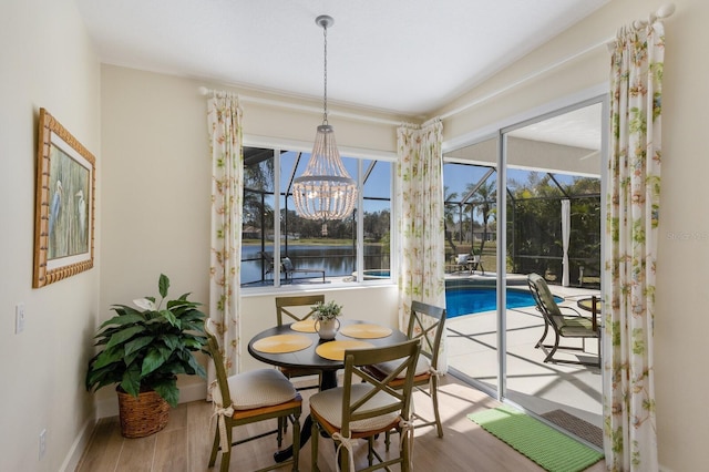 dining area featuring an inviting chandelier, a water view, baseboards, and wood finished floors