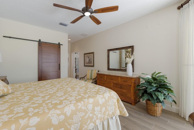 bedroom with ceiling fan, a barn door, visible vents, and light wood-style floors