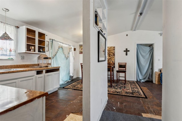 kitchen featuring stone tile floors, white cabinets, hanging light fixtures, vaulted ceiling with beams, and a sink