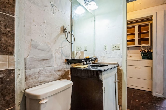 half bathroom with toilet, washer / dryer, vanity, and tile walls