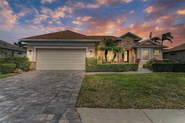 ranch-style home featuring decorative driveway, stucco siding, an attached garage, stone siding, and a front lawn