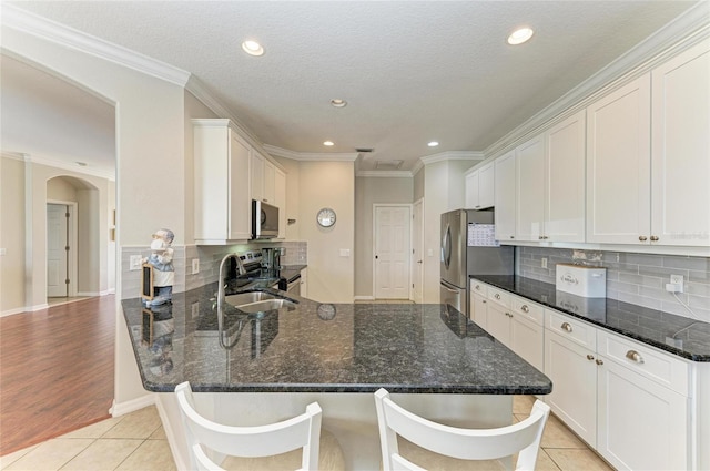 kitchen featuring light tile patterned floors, arched walkways, a peninsula, stainless steel appliances, and a sink