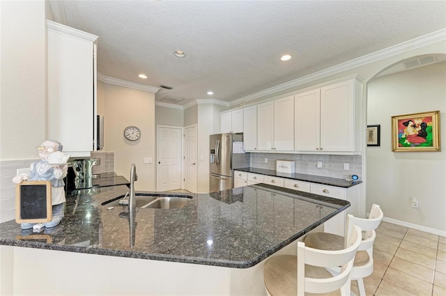 kitchen with stainless steel refrigerator with ice dispenser, tasteful backsplash, white cabinetry, a sink, and a peninsula