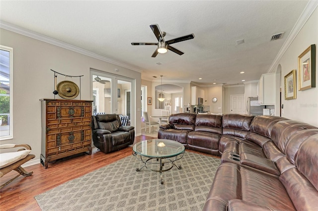 living room with a textured ceiling, arched walkways, wood finished floors, visible vents, and ornamental molding