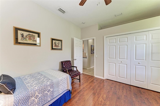 bedroom with ceiling fan, wood finished floors, visible vents, baseboards, and a closet