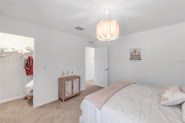 bedroom with baseboards, a walk in closet, visible vents, and light colored carpet