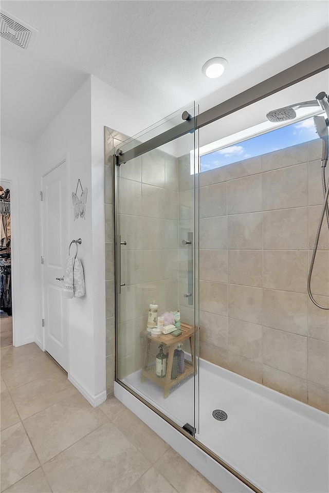 bathroom with a walk in closet, visible vents, a stall shower, tile patterned flooring, and baseboards