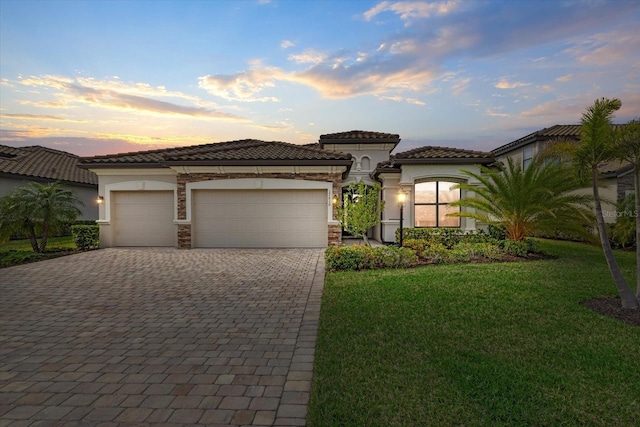 mediterranean / spanish-style house featuring a garage, decorative driveway, a front yard, and stucco siding