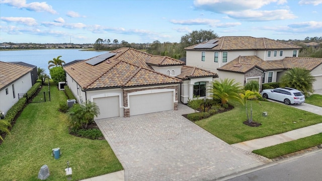 view of front of house featuring a garage, a water view, a tile roof, decorative driveway, and roof mounted solar panels