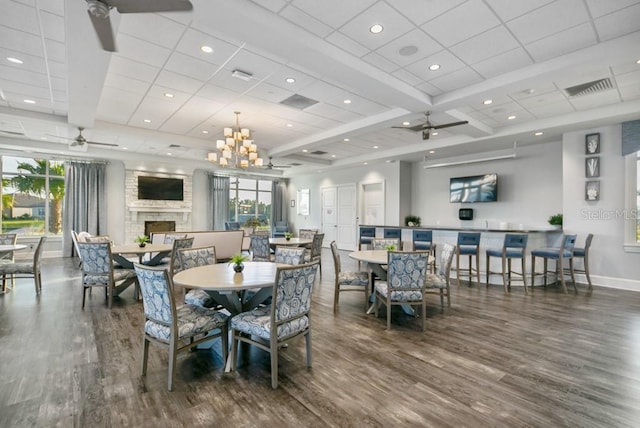 dining area featuring dark wood-style floors, a large fireplace, a ceiling fan, and baseboards