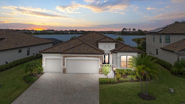 view of front of home with a garage, a tiled roof, a water view, decorative driveway, and a front lawn