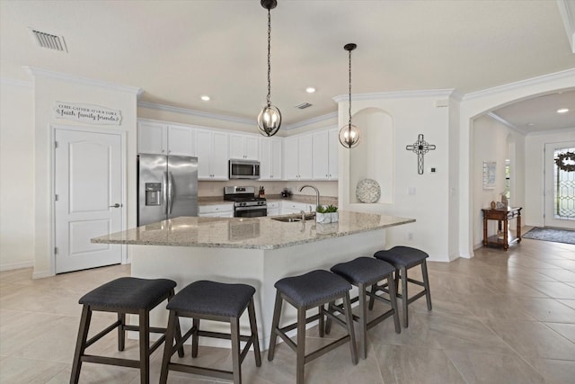 kitchen with arched walkways, appliances with stainless steel finishes, a kitchen breakfast bar, white cabinetry, and a sink