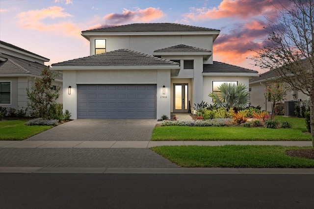 view of front facade featuring a garage, central AC unit, decorative driveway, and stucco siding