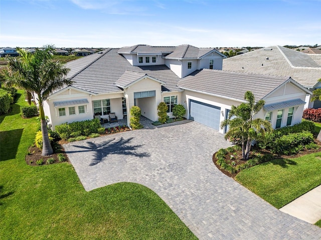 view of front of property with decorative driveway, stucco siding, a garage, a tiled roof, and a front lawn