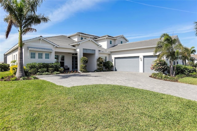 view of front of house featuring a tile roof, an attached garage, decorative driveway, a front yard, and stucco siding