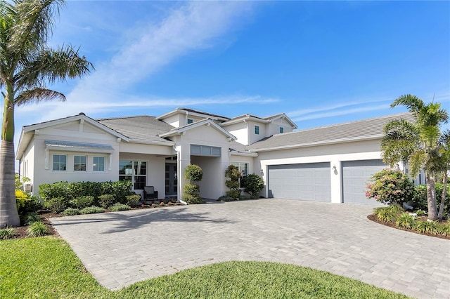 view of front of property featuring a garage, decorative driveway, a tiled roof, and stucco siding