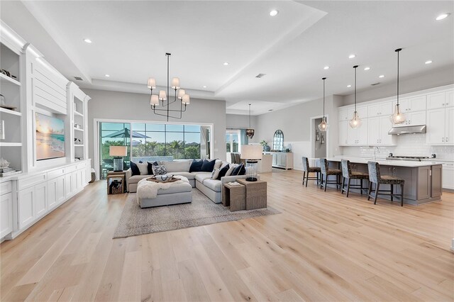 living room with a notable chandelier, a raised ceiling, light wood-style flooring, and recessed lighting