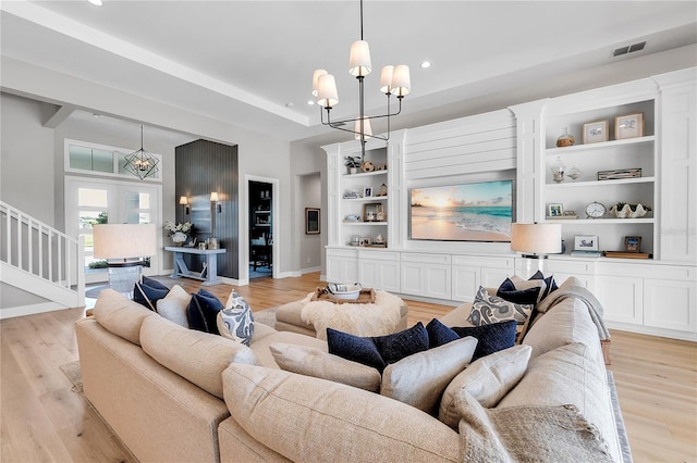 living area featuring baseboards, a tray ceiling, light wood-style floors, built in shelves, and a notable chandelier