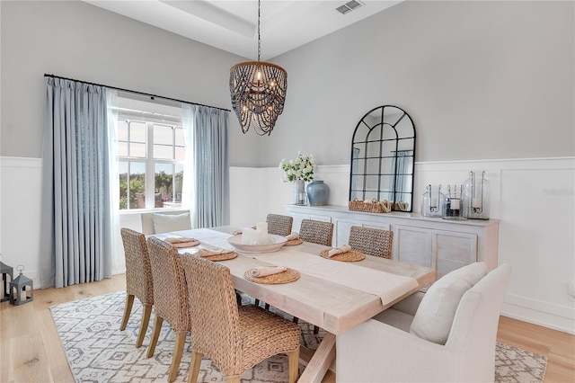 dining room featuring light wood-type flooring, an inviting chandelier, visible vents, and wainscoting