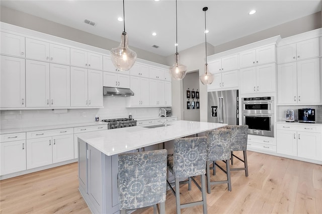 kitchen with decorative backsplash, appliances with stainless steel finishes, a sink, under cabinet range hood, and a kitchen breakfast bar