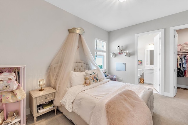 bedroom featuring light carpet, a spacious closet, baseboards, and ensuite bathroom