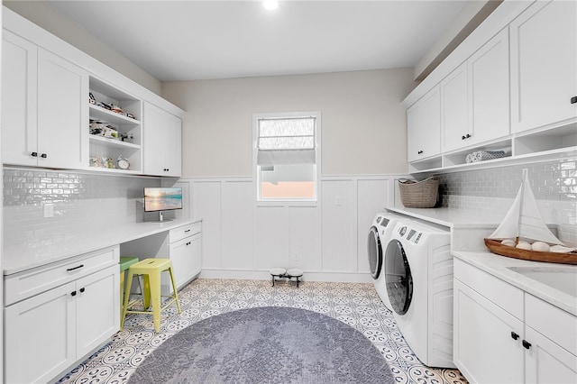 clothes washing area featuring cabinet space, washing machine and dryer, and a wainscoted wall