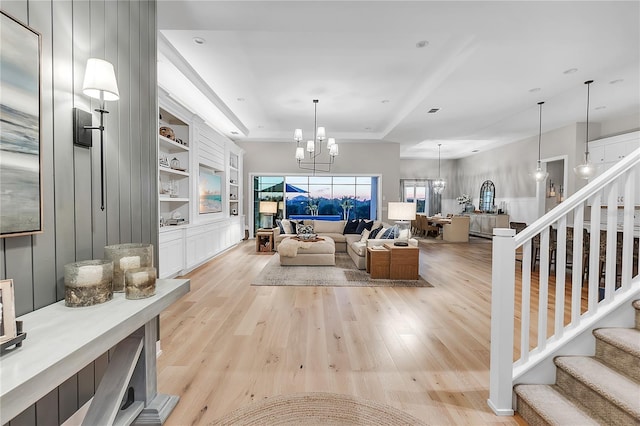 living room featuring built in shelves, light wood-type flooring, a notable chandelier, and stairs