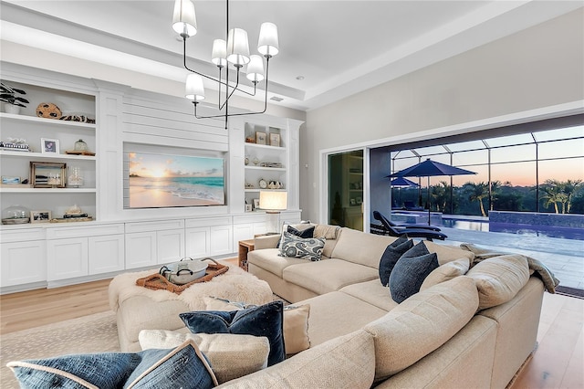 living area with built in shelves, a tray ceiling, light wood-style floors, a sunroom, and a chandelier