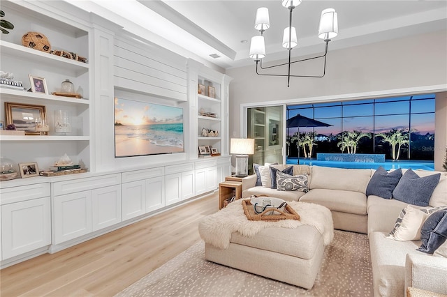 living room with an inviting chandelier, built in shelves, visible vents, and light wood finished floors