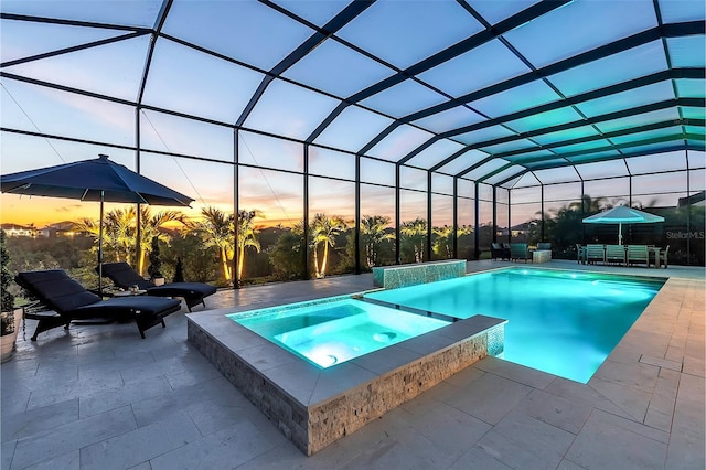 pool at dusk with a pool with connected hot tub, glass enclosure, and a patio