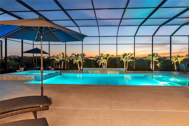 pool at dusk featuring glass enclosure, a pool with connected hot tub, and a patio area