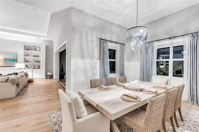 dining area featuring a chandelier, light wood-type flooring, a towering ceiling, and built in features