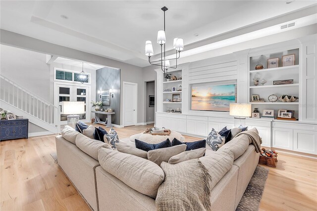 living room with built in features, a notable chandelier, visible vents, stairway, and light wood-style floors