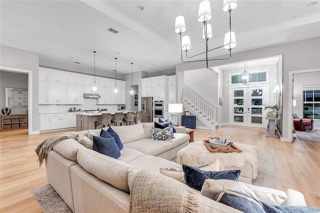 living room with an inviting chandelier, stairs, visible vents, and light wood finished floors