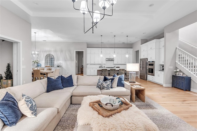 living room with stairs, light wood-style floors, and a notable chandelier