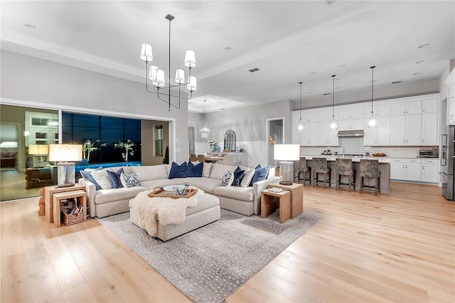 living area with light wood-style floors, visible vents, and an inviting chandelier