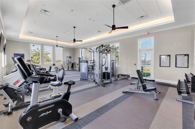 gym with a ceiling fan, a tray ceiling, visible vents, and baseboards