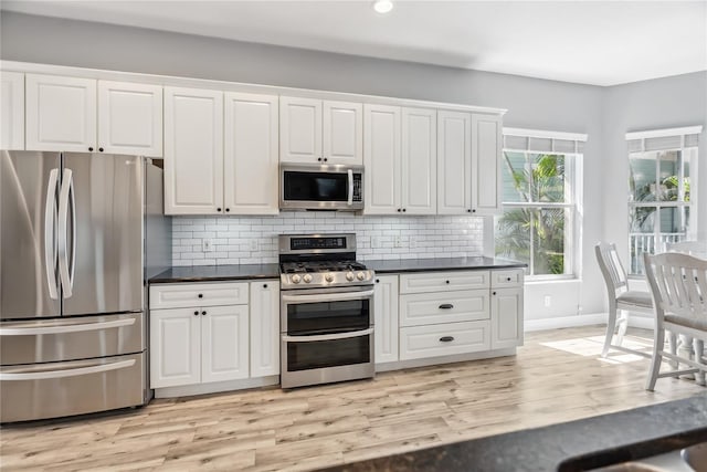 kitchen with dark countertops, stainless steel appliances, light wood-style floors, white cabinets, and decorative backsplash