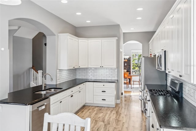 kitchen featuring a peninsula, a sink, white cabinets, appliances with stainless steel finishes, and dark countertops