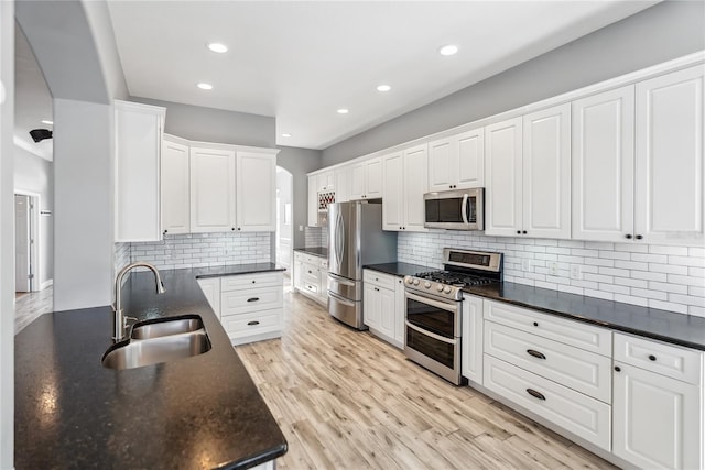 kitchen featuring light wood finished floors, white cabinets, stainless steel appliances, and a sink