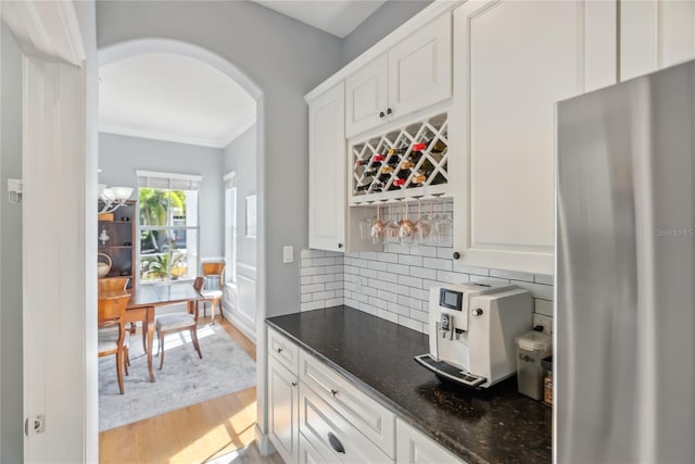 kitchen featuring backsplash, dark stone countertops, freestanding refrigerator, light wood-style floors, and arched walkways