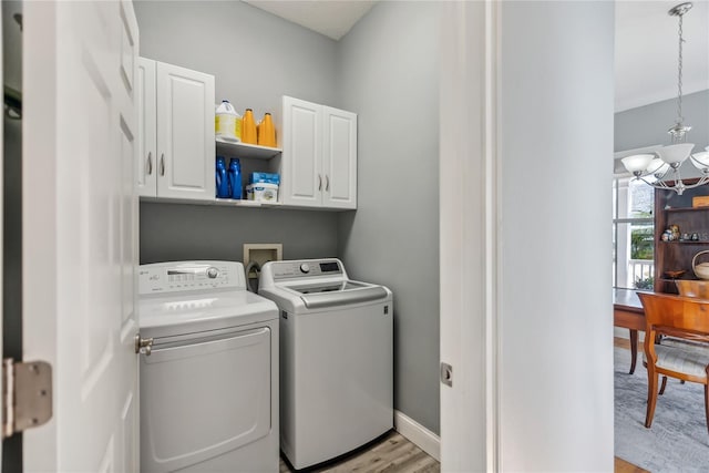 laundry area featuring washer and dryer, cabinet space, an inviting chandelier, light wood finished floors, and baseboards