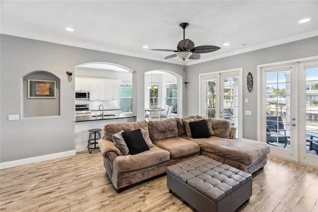 living area featuring arched walkways, light wood-style flooring, baseboards, and ceiling fan