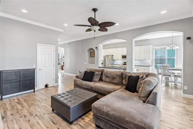 living area featuring crown molding, ceiling fan with notable chandelier, arched walkways, and light wood finished floors