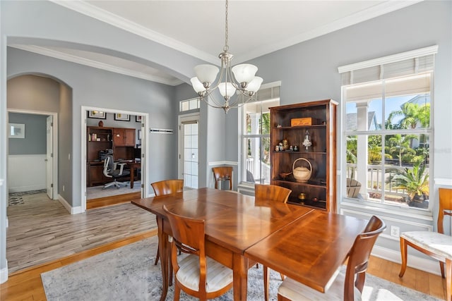 dining area with a wealth of natural light, arched walkways, a chandelier, and light wood finished floors