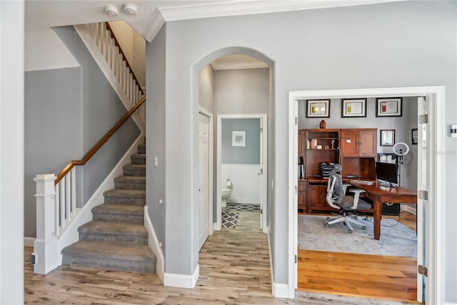 entrance foyer featuring light wood-type flooring, ornamental molding, stairway, arched walkways, and baseboards